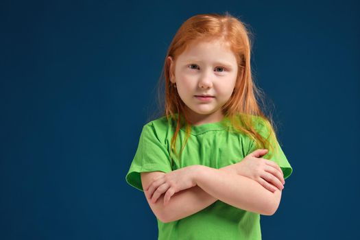 close up photo of little redhead emotional girl in green t-shirt posing before camera. She shows mistrust and shyness