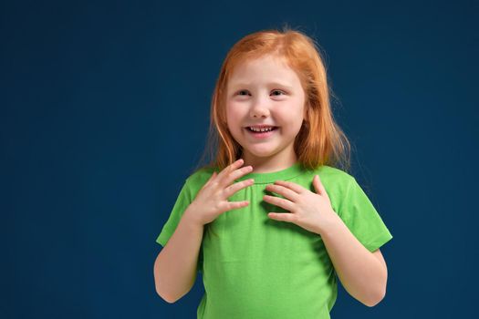 Cute little girl, in green t-shirt surprised by something, she feels emotional lift, blue background