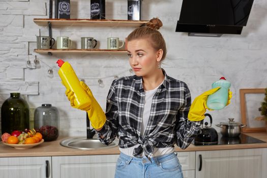 Woman comparing detergent products, she is holding two bottles and checking them at home kitchen. Household, cleaning and people concept
