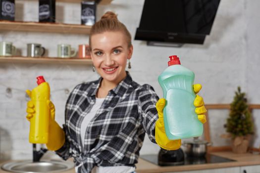 Woman comparing detergent products, she is holding two bottles and checking them at home kitchen. Household, cleaning and people concept