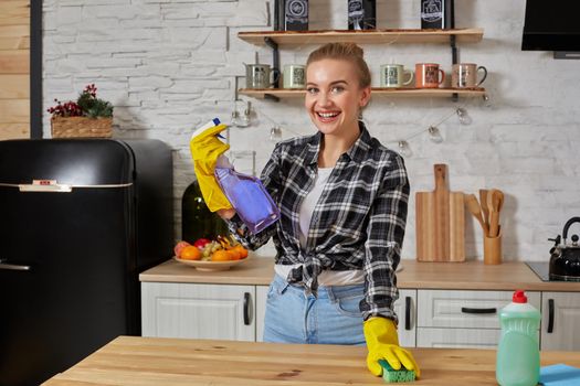 Beautiful woman in protective gloves cleaning kitchen table with rag and spray. Household, cleaning and people concept