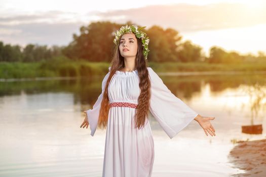 Beautiful black haired girl in white vintage dress and wreath of flowers standing in water of lake. Fairytale story. Warm art work. Sun flare