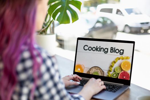 Back view of young pink hair woman watching blog video about healthy food on laptop while sitting in cafe