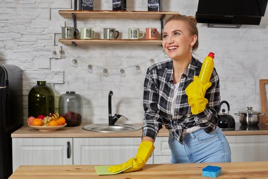 Household, cleaning and people concept - happy woman or housewife in rubber gloves wiping table with microfiber cloth at home kitchen.
