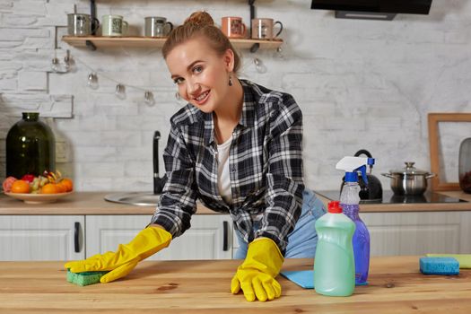 Household, cleaning and people concept - happy woman or housewife in rubber gloves wiping table with microfiber cloth at home kitchen.