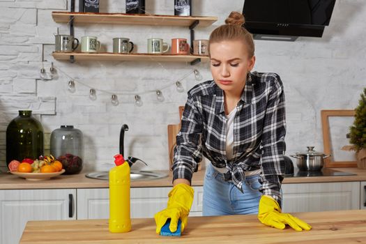 Young woman in protective gloves wipes a table in the kitchen with a rag. Fatigue. Household, cleaning and people concept