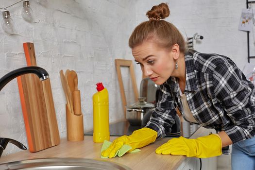 Hand cleaning. Young housewife woman washing sink in kitchen. Young woman washing manually, by hand, wearing yellow cleaning rubber gloves.