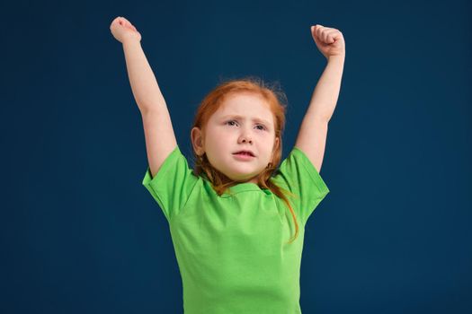 close up photo of little redhead emotional girl in green t-shirt posing before camera.She is tired and wants to sleep, yawning and stretching