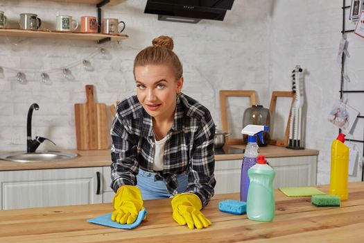 Household, cleaning and people concept - happy woman or housewife in rubber gloves wiping table with microfiber cloth at home kitchen.