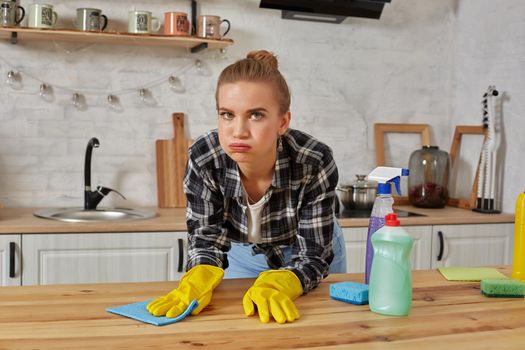 Young woman in protective gloves wipes a table in the kitchen with a rag. Fatigue. Household, cleaning and people concept