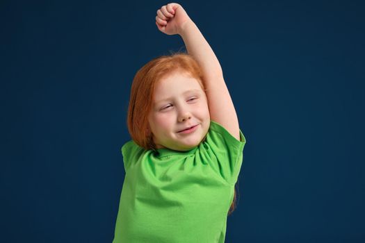 close up photo of little redhead emotional girl in green t-shirt posing before camera.She is tired and wants to sleep, yawning and stretching