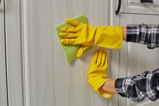 Hands in gloves with green rag is cleaning kitchen cabinets - housework and housekeeping concept. Close-up