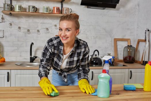 Household, cleaning and people concept - happy woman or housewife in rubber gloves wiping table with microfiber cloth at home kitchen.