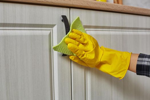 Hands in gloves with green rag is cleaning kitchen cabinets - housework and housekeeping concept. Close-up