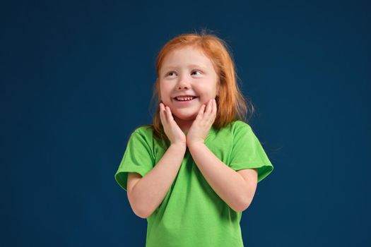 Cute little girl, in green t-shirt surprised by something, she feels emotional lift, blue background