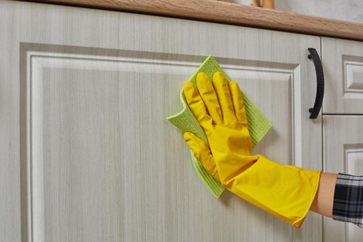 Hands in gloves with green rag is cleaning kitchen cabinets - housework and housekeeping concept. Close-up