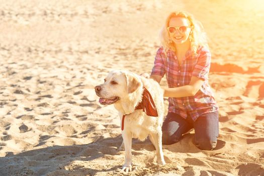 Portrait of young beautiful woman in sunglasses sitting on sand beach with golden retriever dog. Girl with dog by sea. Happiness and friendship. Pet and woman. Woman playing with dog on sea shore. Sun flare