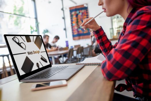 Cropped shot view of young woman working on laptop computer while sitting in modern cafe bar interior, female freelancer using net-book for remote job during morning breakfast in coffee shop. Design. Web design