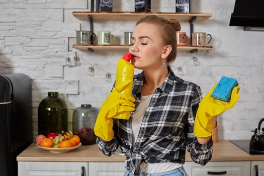 Housekeeper concept. Professional young woman wearing rubber protective yellow gloves holding bottle cleaners in the kitchen. Housewife hold bottle spray work clean at home.