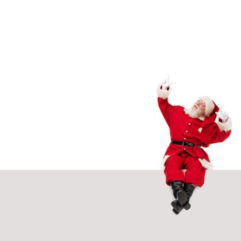 Santa Claus sitting on a blank panel and pointing up isolated on white background