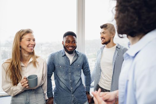 Cheerful young business people have a talk during coffee break in office near window