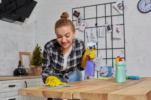Household, cleaning and people concept - happy woman or housewife in rubber gloves wiping table with microfiber cloth at home kitchen.