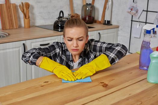 Young woman in protective gloves wipes a table in the kitchen with a rag. Fatigue. Household, cleaning and people concept