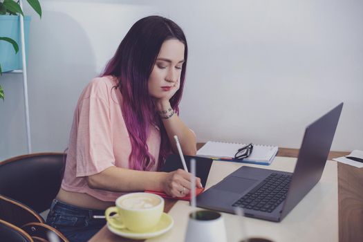 Young woman with pink hair with laptop computer sitting in cafe, intelligent female student working on net-book after her lectures in University