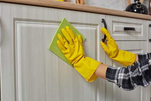 Hands in gloves with green rag is cleaning kitchen cabinets - housework and housekeeping concept. Close-up