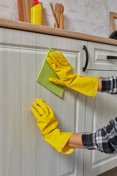 Hands in gloves with green rag is cleaning kitchen cabinets - housework and housekeeping concept. Close-up