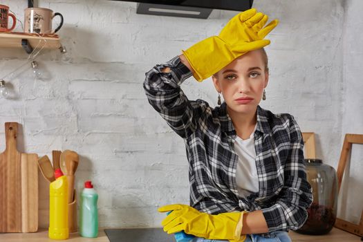 Blonde woman in protective gloves with rag cleaning electric stove at home kitchen. Girl washing black shiny surface of kitchen top. Concept of housework.