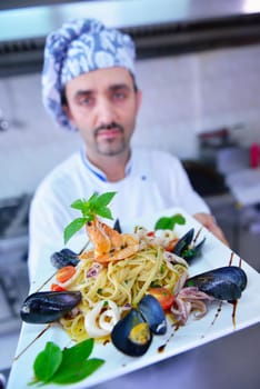 Handsome chef dressed in white uniform decorating pasta salad and seafood fish in modern kitchen