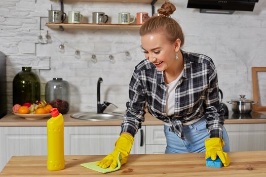 Household, cleaning and people concept - happy woman or housewife in rubber gloves wiping table with microfiber cloth at home kitchen.