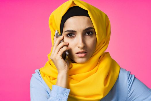 muslim woman in yellow hijab talking on the phone pink technology background. High quality photo