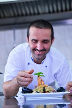 Handsome chef dressed in white uniform decorating pasta salad and seafood fish in modern kitchen