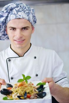 Handsome chef dressed in white uniform decorating pasta salad and seafood fish in modern kitchen