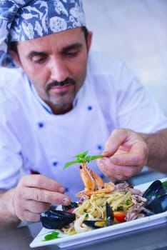 Handsome chef dressed in white uniform decorating pasta salad and seafood fish in modern kitchen