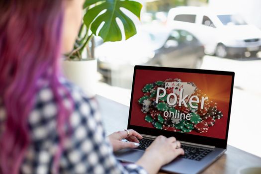 Back view of a young pink hair woman keyboarding on laptop computer with poker online on a screen while sitting in cafe. Play online concept. Screen graphics are made up.