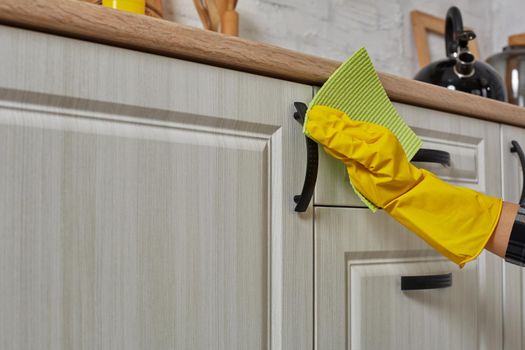 Hands in gloves with green rag is cleaning kitchen cabinets - housework and housekeeping concept. Close-up