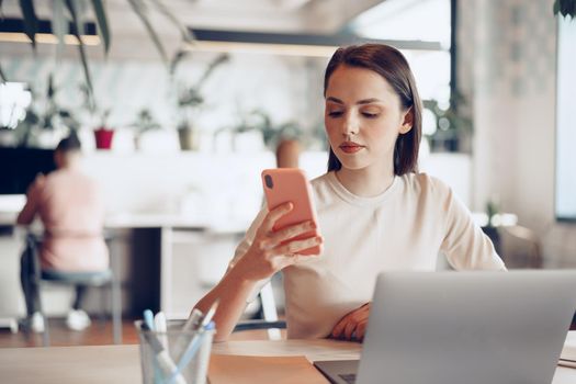 Young attractive businesswoman using her smartphone in office close up