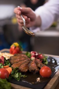 Chef hand finishing steak meat plate with Finally dish dressing and almost ready to serve at the table