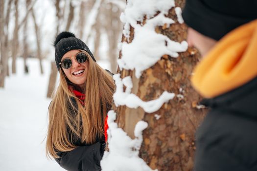 Young loving couple play hide and seek in a snowy winter park close up