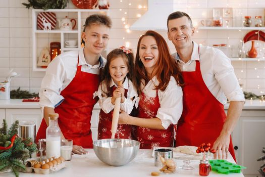 A happy family is standing in the Christmas kitchen and preparing dough for making cookies.