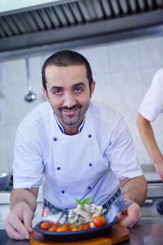 Handsome chef dressed in white uniform decorating pasta salad and seafood fish in modern kitchen