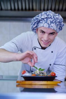 Handsome chef dressed in white uniform decorating pasta salad and seafood fish in modern kitchen