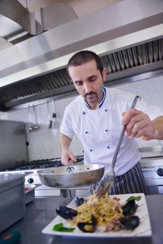 Handsome chef dressed in white uniform decorating pasta salad and seafood fish in modern kitchen