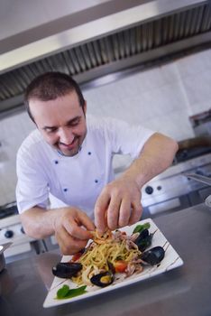 Handsome chef dressed in white uniform decorating pasta salad and seafood fish in modern kitchen