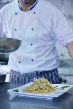 Handsome chef dressed in white uniform decorating pasta salad and seafood fish in modern kitchen