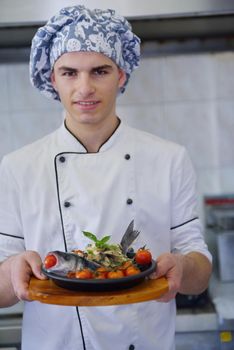 Handsome chef dressed in white uniform decorating pasta salad and seafood fish in modern kitchen