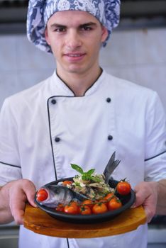 Handsome chef dressed in white uniform decorating pasta salad and seafood fish in modern kitchen